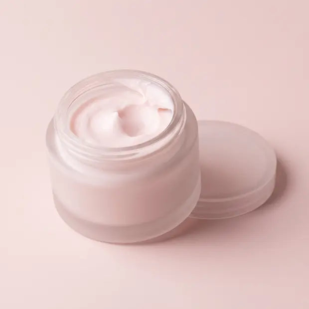 An open cosmetic jar with its lid lifted off and a scoop taken out of the cream